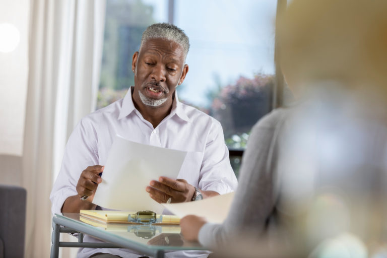 Senior male therapist reading from a paper at a desk