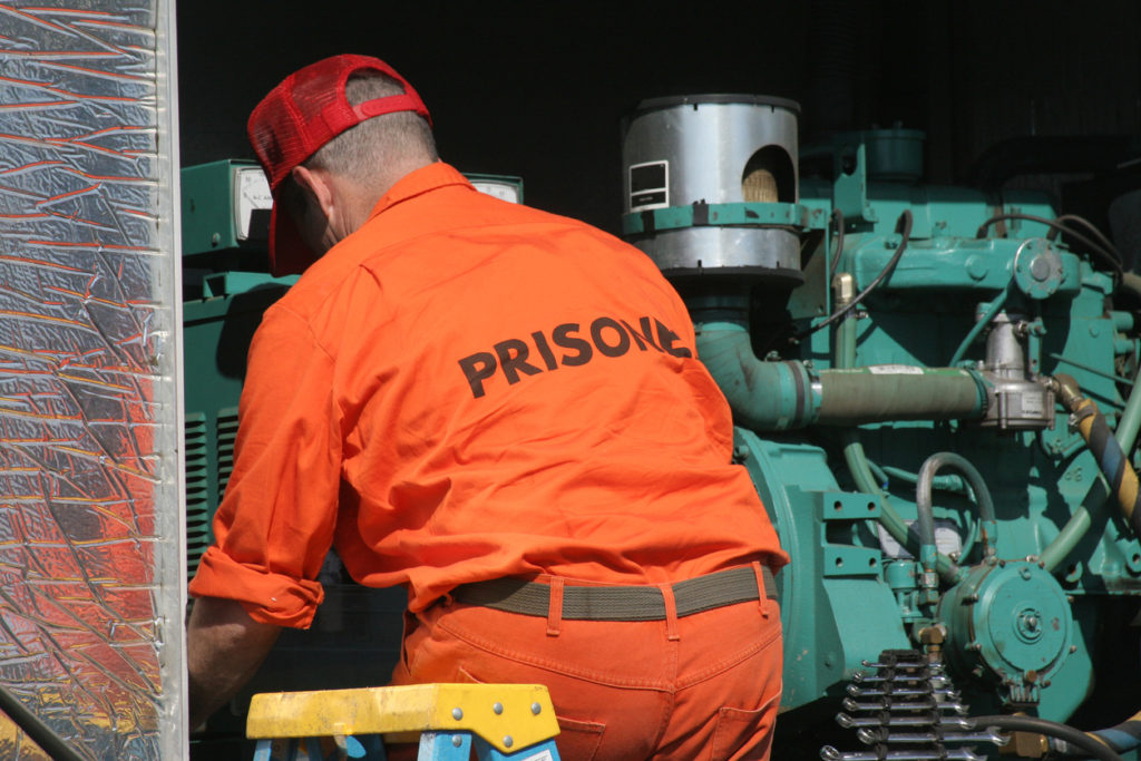 a man in orange prisoner clothes working on a machine